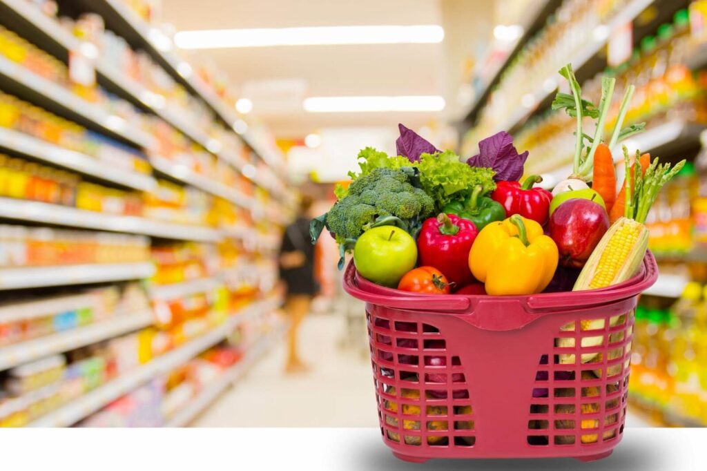 A red basket full of fresh fruit and vegetables in a grocery store.