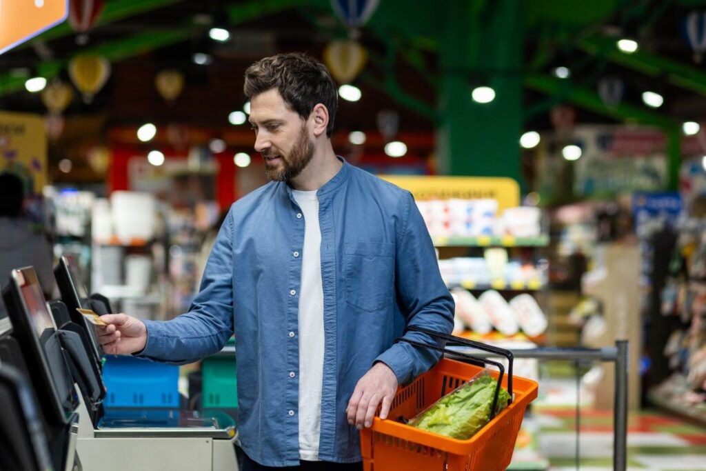 A man in a blue shirt purchasing lettuce at a self-checkout.