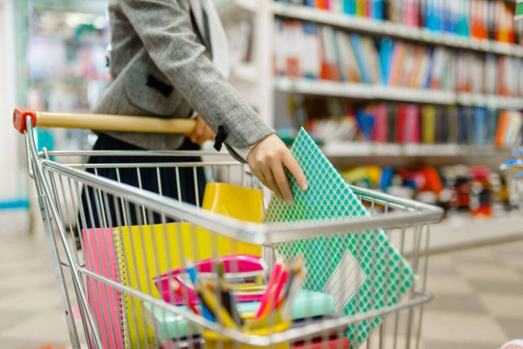 A person filling a shopping cart with school supplies in a store.