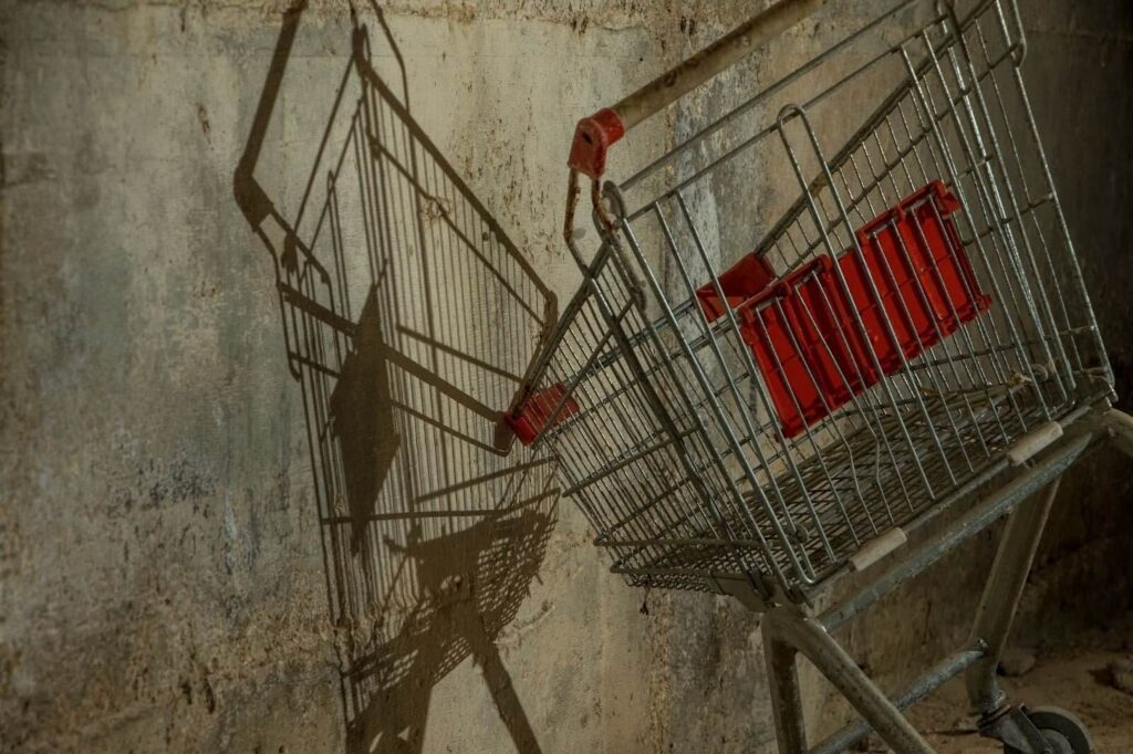 A shopping cart leaning against a cement wall, casting a shadow.