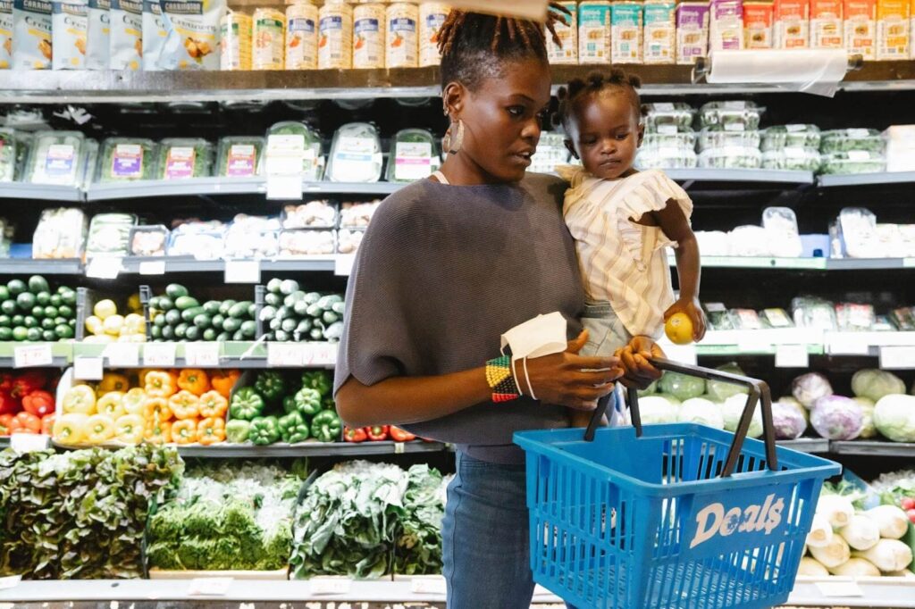 A woman holding a shopping basket and her kid in a grocery store.