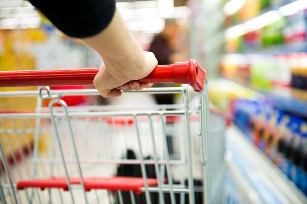 A hand gripping an empty shopping cart in a blurred grocery aisle.