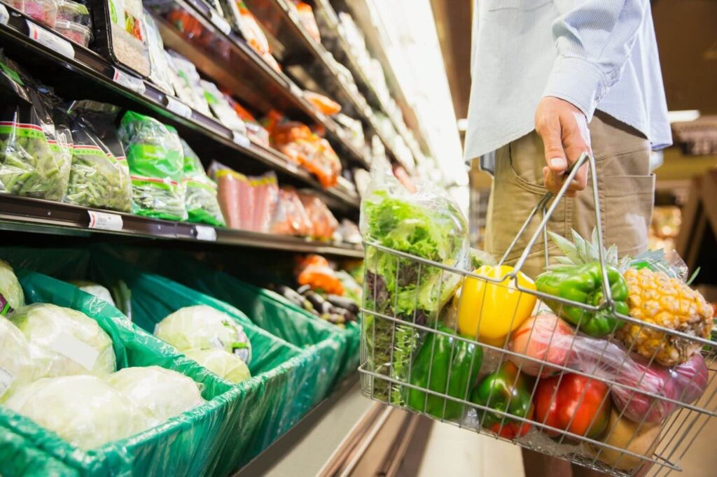 A grocery basket filled with pineapple, bell peppers, and lettuce in a store aisle.