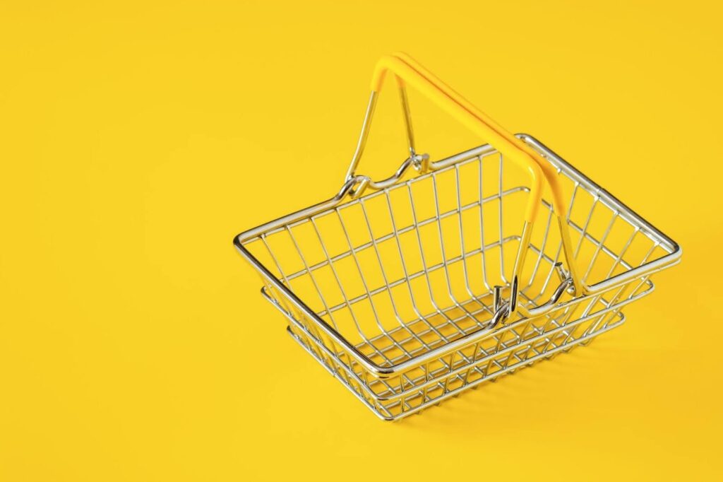 A small empty wire shopping basket on a yellow background.