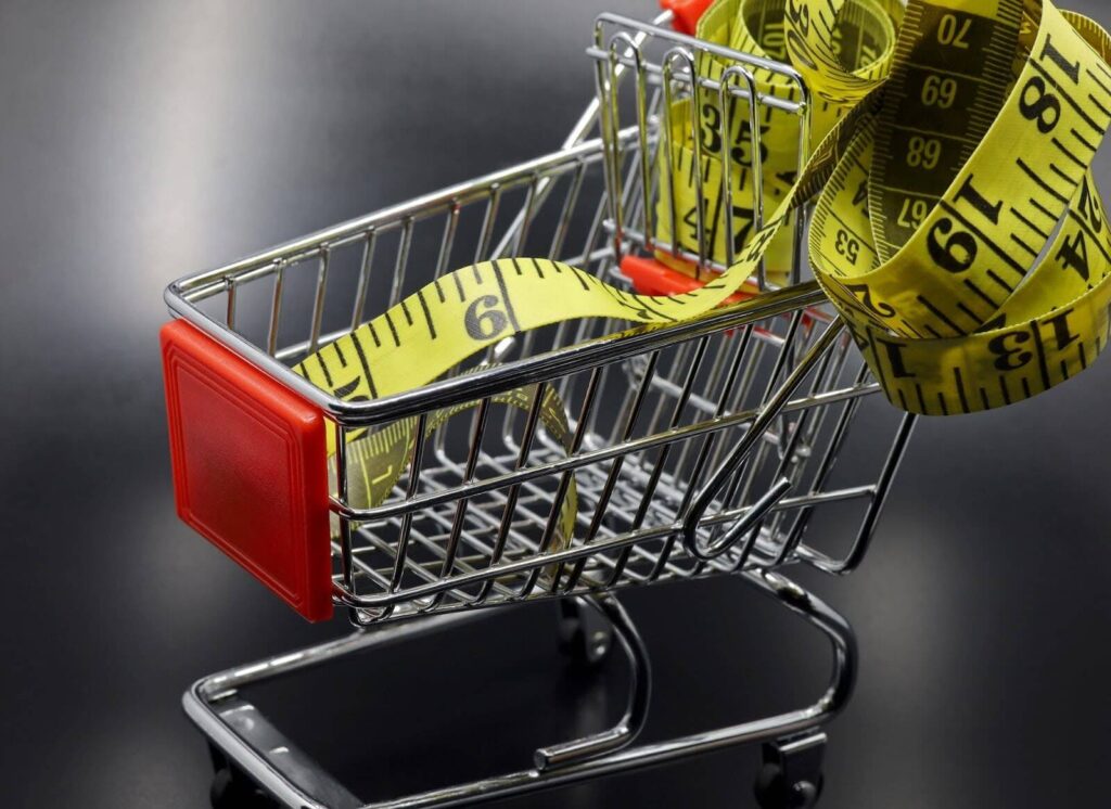 Close up of a miniature shopping cart with yellow measuring tape.