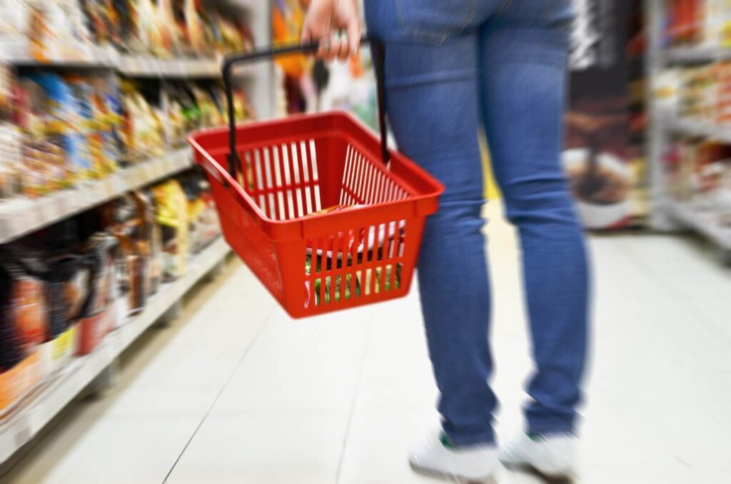 A person in jeans holding a red shopping basket in a grocery aisle.