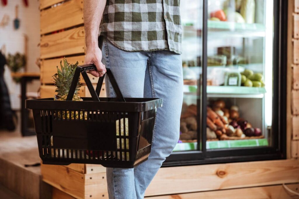 A person in jeans holding a shopping basket in a grocery store.