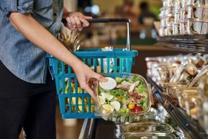 Customer choosing salad produckt with blue medium sized plastick basket